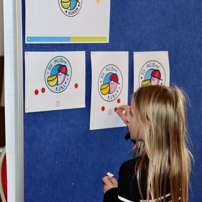Bild vergr&ouml;&szlig;ern: An einer Wand sind verschiedene Logos angebracht. Davor steht ein Mädchen und stimmt für ihren Favoriten.