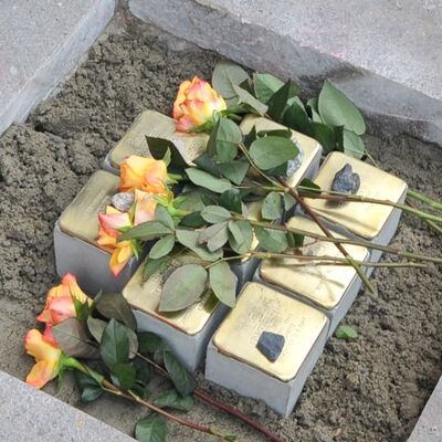Mehrere Steine auf einem Gehweg eingearbeitet und darauf sind Blumen abgelegt.