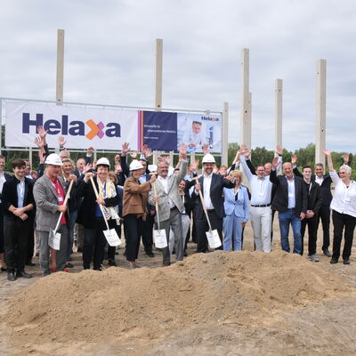 Foto: Zahlreiche Menschen auf einer Baustelle vor einem Banner mit der Aufschrift Helaxa.