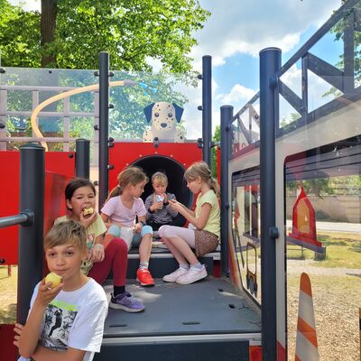 Bild vergr&ouml;&szlig;ern: Foto: Eine Gruppe Kinder isst und trinkt auf einem Spielgerät.