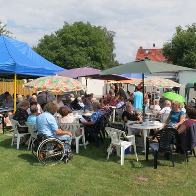 Viele Menschen sitzen in Stühlen und Rollstühlen um Tische, trinken Kaffee, essen Kuchen, erzählen miteinander.