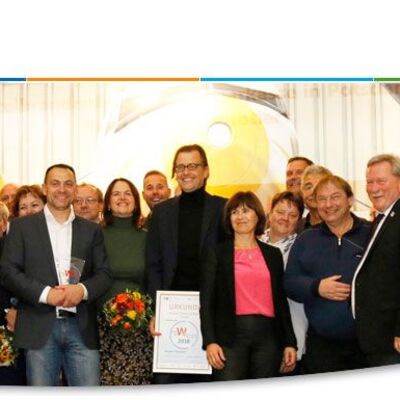 Etliche Menschen stehen nebeneinander und lächeln in die Kamera. Einige halten Blumensträuße und Urkunden. Links oben steht "Wirtschaftswoche Teltow-Fläming 2019". Rechts unten steht "4. bis 10. November 2019".