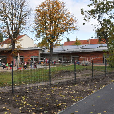 Foto: evangelische Kita - Holzgebäude und davor Grünfläche mit Bäumen