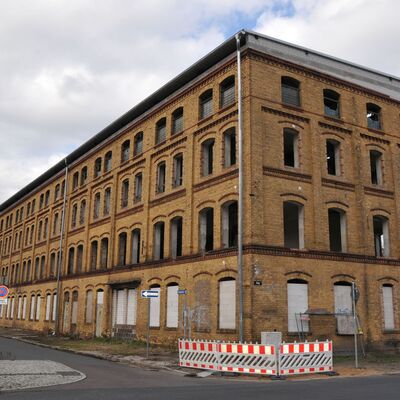 Foto: Ein großes Gebäude aus gelbem Backstein an einer Straßenkreuzung. 