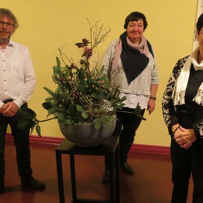 ein Mann und zwei Frauen stehen in einem Flur um ein Blumengesteck herum