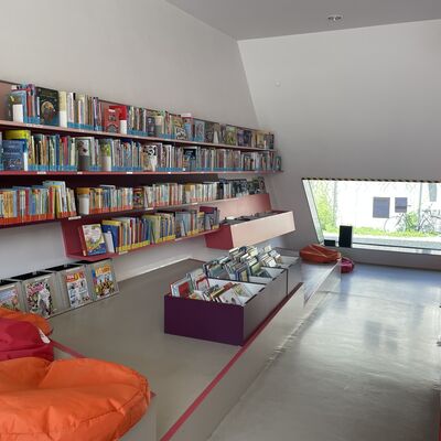 Das Bild zeigt das Innere der Bibliothek im Bahnhof. Zu sehen sind Bücherregale, eine Sitzmöglichkeit und ein Fenster.