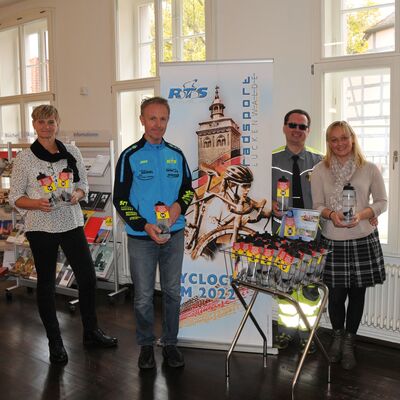 Foto: Zwei Frauen und zwei Männer stehen vor einem Veranstaltungsbanner und halten Trinkflaschen.