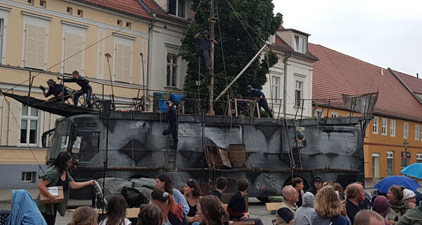 Bild vergr&ouml;&szlig;ern: Foto: Publikum vor der Kulisse eines großen Schiffs.