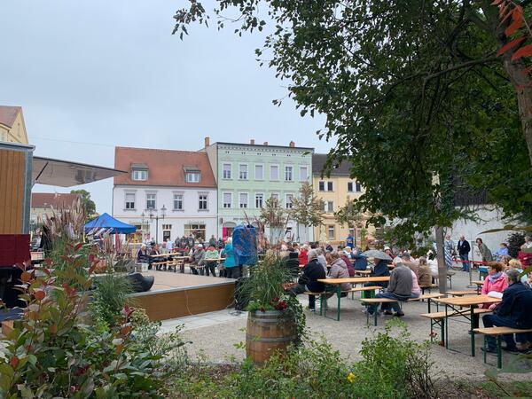 Bild vergr&ouml;&szlig;ern: Foto: Publikum sitzt vor einer kleinen Bühne.