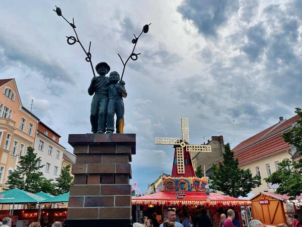 Bild vergr&ouml;&szlig;ern: Foto: Zwei Steinfiguren vor beleuchteten Essensständen