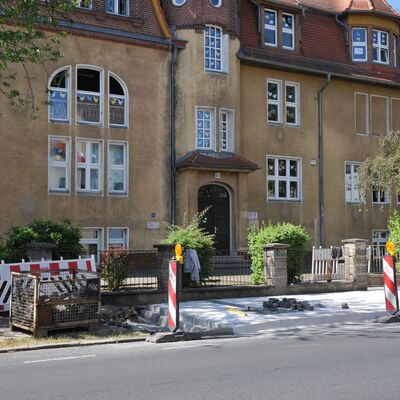 Foto: Eine Baustelle an einer Bushaltestelle vor einem Schulgebäude.