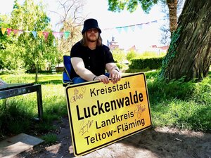 Bild vergr&ouml;&szlig;ern: Ein junger Mann posiert mit Ortsschild.