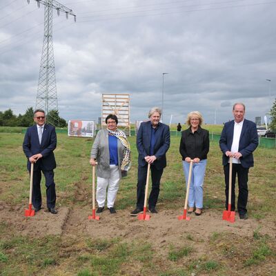 Foto: Zwei Frauen und drei Männer stehen mit roten Spaten auf einem Grundstück.