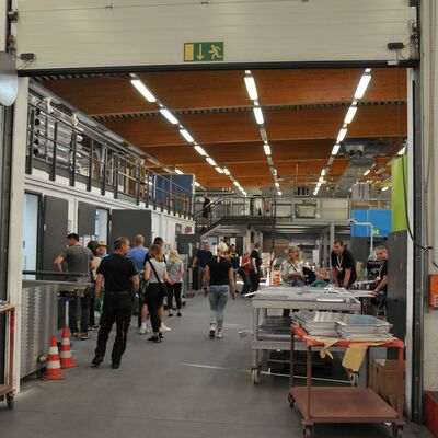 Foto: Blick in eine Produktionshalle, in der Menschen umherlaufen.