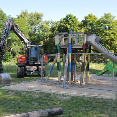 Bild vergr&ouml;&szlig;ern: Foto: Ein Spielplatz hinter einem Bauzaun, daneben ein Bagger.