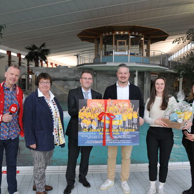 Foto: Drei Männer und drei Frauen stehen vor einem Schwimmbecken in einem Hallenbad. Zwei Männer halten ein großes Bild mit einer Schleife, eine Frau einen Geschenkkorb.