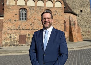 Bild vergr&ouml;&szlig;ern: Ein Mann im Anzug steht vor einem historischem Gebäude.