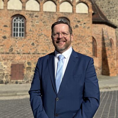 Ein Mann im Anzug steht vor einem historischem Gebäude.