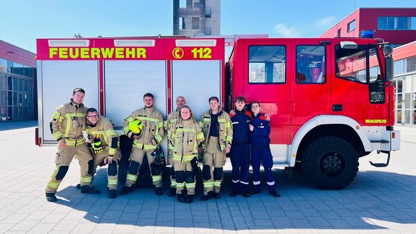 Bild vergr&ouml;&szlig;ern: Feuerwehrleute stehen vor einem Einsatzfahrzeug.