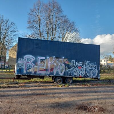 Foto: Ein alter, beschmierter LKW-Anhänger vor Bäumen.