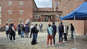 Bild vergr&ouml;&szlig;ern: Foto: Zahlreiche Menschen vor einem großen Backsteingebäude.