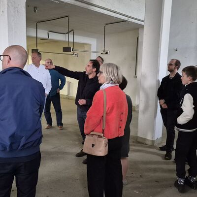 Bild vergr&ouml;&szlig;ern: Foto: Zahlreiche Menschen in einem großen, weißen Raum. Ein Mann in der Mitte zeigt auf etwas.