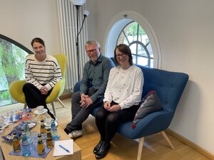 Bild vergr&ouml;&szlig;ern: Foto: Zwei Frauen und ein Mann sitzen auf farbigen Sesseln zusammen um einen Tisch.