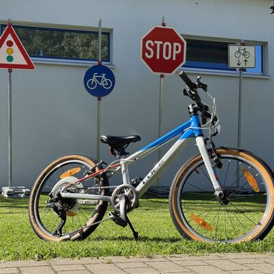 Ein Fahrrad steht auf einer Wiese. Im Hintergrund sind verschiedene Verkehrszeichen aufgestellt.