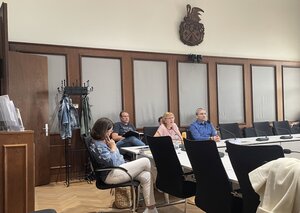 Bild vergr&ouml;&szlig;ern: Foto: Menschen sitzen in einem Saal an einem Tisch.