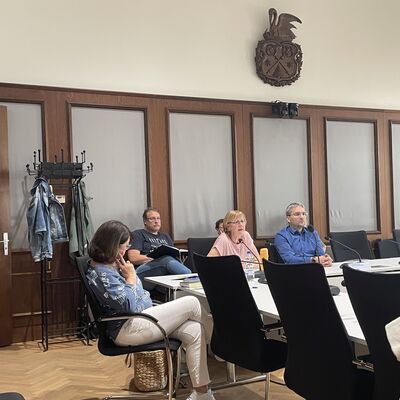 Foto: Menschen sitzen in einem Saal an einem Tisch.