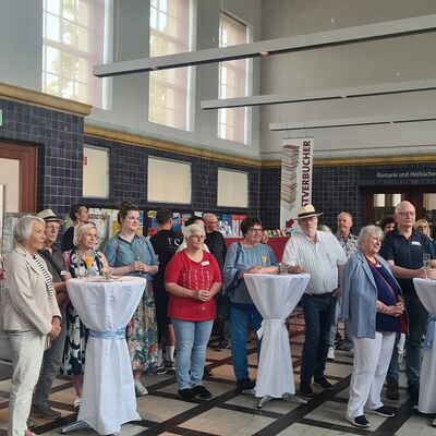 Foto: Zahlreiche Menschen stehen an Stehtischen in einer großen Halle.