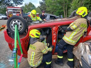 Bild vergr&ouml;&szlig;ern: Foto: Menschen in Einsatzkleidung um ein Auto in Dachlage herum.