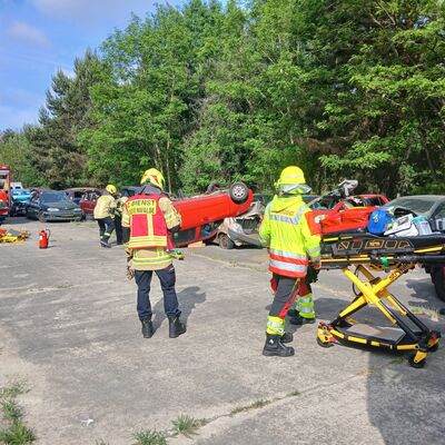Bild vergr&ouml;&szlig;ern: Foto: Menschen in Einsatzkleidung auf einem Parkplatz. Rechts steht eine Rettungsliege.