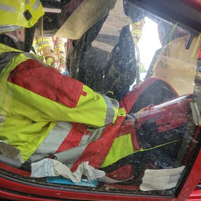 Bild vergr&ouml;&szlig;ern: Foto: Ein Mensch in Einsatzklamotten eingequetscht in ein Fahrzeug.