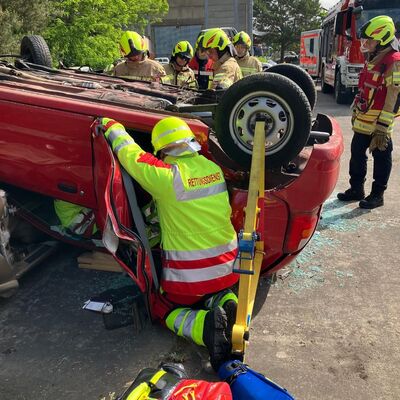 Bild vergr&ouml;&szlig;ern: Foto: Zahlreiche Menschen in Einsatzkleidung. Ein roter PKW liegt auf dem Dach.