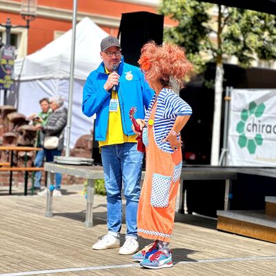 Bild vergr&ouml;&szlig;ern: Auf einer Bühne stehen ein Moderator und eine Frau, die als Clown verkleidet ist.