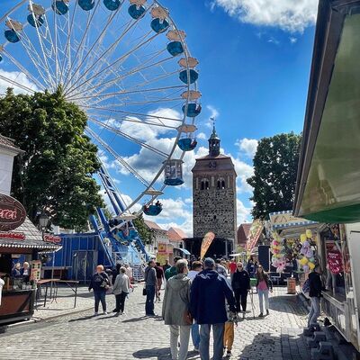 Bild vergr&ouml;&szlig;ern: Ein Riesenrad vor einem Turm und Menschen davor.