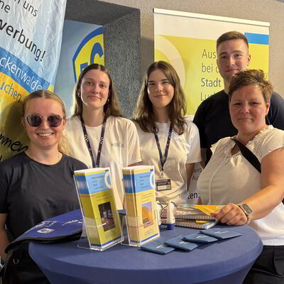 Fünf Personen stehen an einem Stand mit Flyern. 