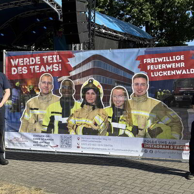 Bild vergr&ouml;&szlig;ern: Zwei Feuerwehrleute stehen an einem Banner.
