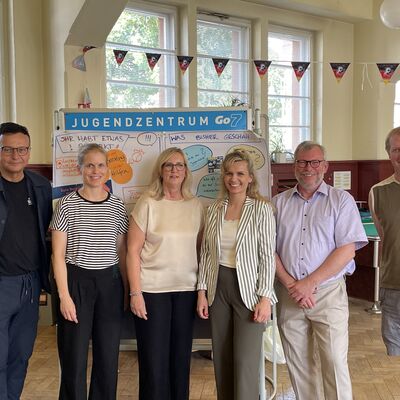 Foto: Drei Frauen und drei Männer stehen vor einer Stellwand in einem geschmückten Saal.