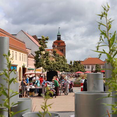 Im Vordergrund sind Metallelemente, die den Bildausschnitt einrahmen. Im Zentrum des Bildes ist Ein Turm vor dem Stände aufgebaut sind.