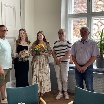 Foto: Zwei Männer und drei Frauen stehen nebeneinander. Zwei der Frauen halten Blumensträuße.