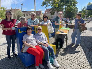 Eine Gruppe von Menschen sitzt auf oder steht neben einer Bank.