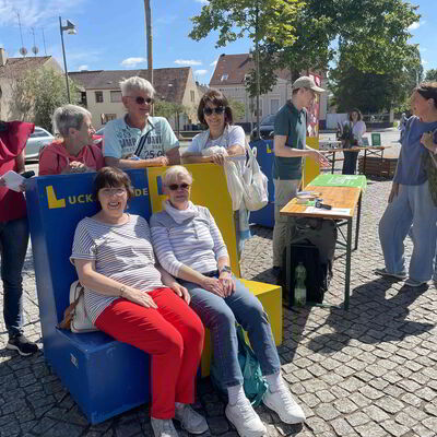 Eine Gruppe von Menschen sitzt auf oder steht neben einer Bank.
