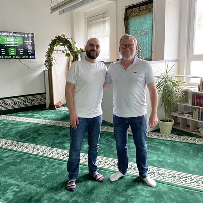 Foto: Zwei Männer stehen in einem Raum mit grünem Teppich.