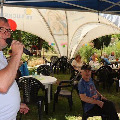Bild vergr&ouml;&szlig;ern: Foto: Ein Mann spricht in ein Mikrofon. Im Hintergrund sitzen Menschen an Tischen.
