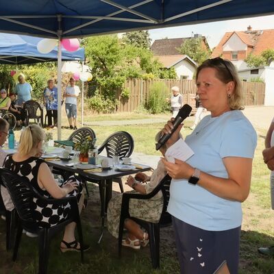 Bild vergr&ouml;&szlig;ern: Foto: Eine Frau spricht in ein Mikrofon. Im Hintergrund sitzen Menschen an Tischen.