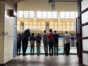 Bild vergr&ouml;&szlig;ern: Mehrere Kinder und ein Erwachsener stehen mit dem Rücken zur Kamera und schauen in ein leeres Schwimmbecken.