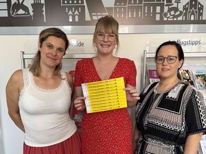 Bild vergr&ouml;&szlig;ern: Drei junge Frauen lächeln in die Kamera. Die mittlere hält Einlassbändchen in der Hand.