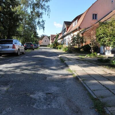 Bild vergr&ouml;&szlig;ern: Foto: Eine unsanierte Straße mit Häusern und Autos am Rand.